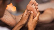 Closeup of masseuse doing foot reflexology to woman at spa. Therapist hands doing foot massage at wellness center. Woman receiving a feet massage at health spa.